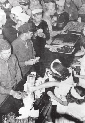 The photograph labeled pheasant canteen shows volunteers serving food cafeteria style to servicemen. Please credit the South Dakota State Historical Society – State Archives. The volunteers would also bring food to the trains and hand the food through open train windows to servicemen and women. The other photo is likely from an ad or poster from the Milwaukee Road.