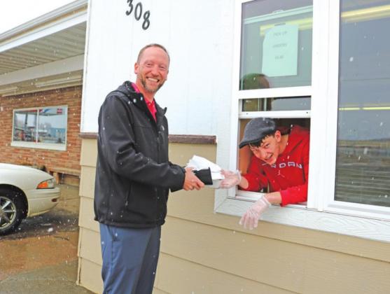 Stockton McClanahan hangs out of the make-shift drive-up window in Hutch’s entryway Thursday while serving John Schlomer of Winner Physical Therapy his lunch order.